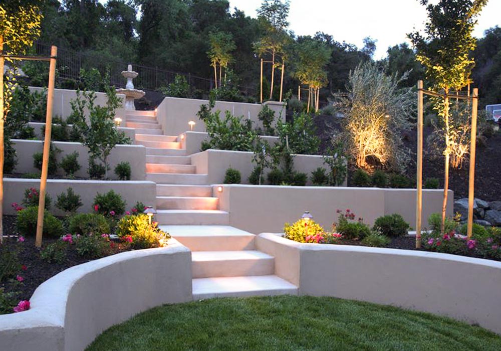 Terraced hardscape garden with tiered planters, illuminated steps, and decorative trees