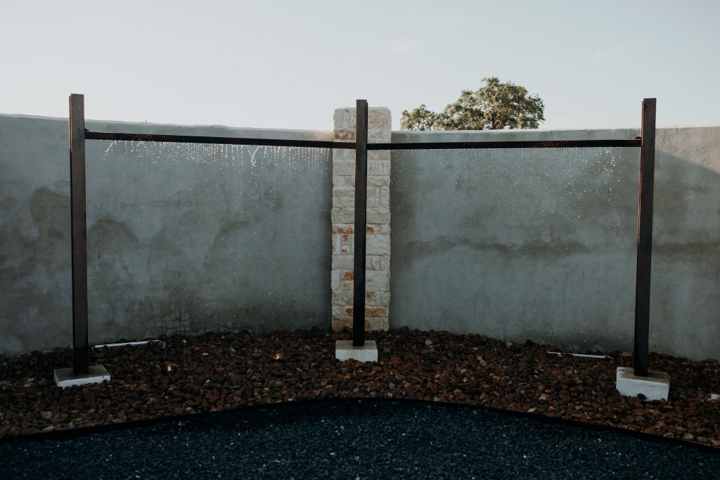 Minimalist water feature with a modern metal and stone design, set against a concrete wall with decorative gravel landscaping