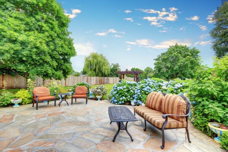 Hardscape patio with cushioned seating, stone flooring, and a vibrant garden featuring hydrangeas