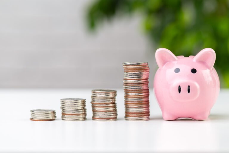 Pink piggy bank next to stacks of coins on a white table, symbolizing saving and financial growth