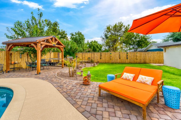 Vibrant backyard with hardscapes, featuring a poolside lounge, wooden pergola, and bright orange seating under an umbrella