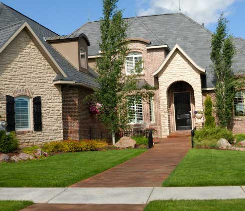 Residential hardscape featuring a brick walkway leading to a stone and brick house