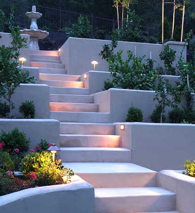 Terraced hardscape garden with tiered planters, illuminated steps, and decorative trees