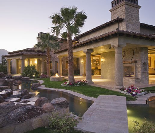 Luxury hardscape featuring a Mediterranean-style villa, outdoor fireplace, stone pathways, and water features with palm trees