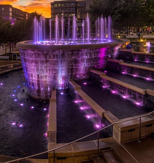 Stunning fountain illuminated by purple lights, set against a beautiful sunset backdrop