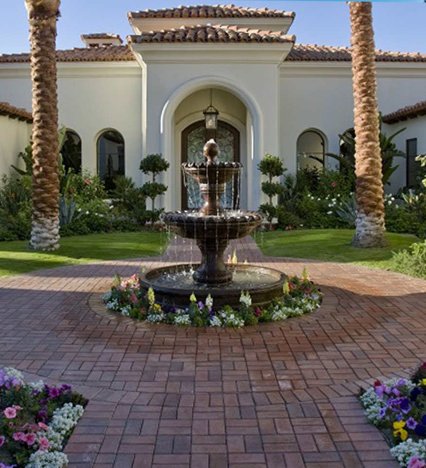 Luxury home entrance featuring an elegant fountain surrounded by beautifully arranged hardscapes and vibrant flowers