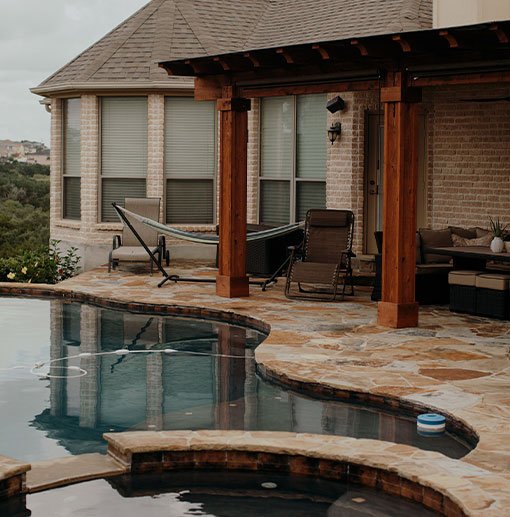 Outdoor space featuring a luxurious pool with hardscapes, complemented by a wooden pergola and comfortable seating