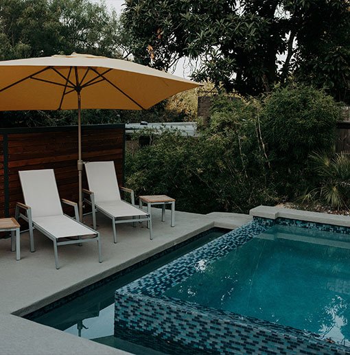 Relaxing poolside area featuring stylish hardscapes with lounge chairs, an umbrella, and a modern plunge pool