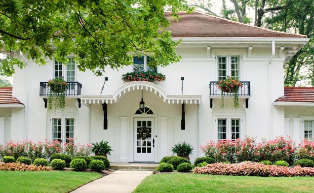 Charming white house featuring a welcoming front porch and a lush garden filled with colorful flowers