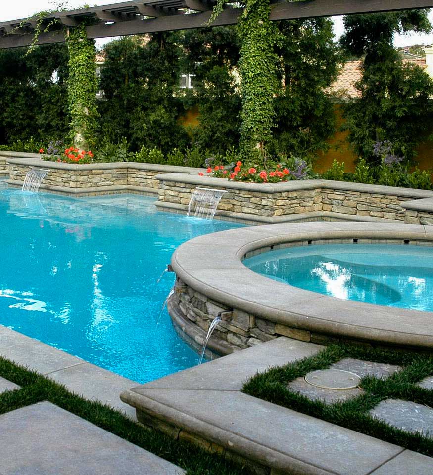 Pool and spa with cascading waterfalls, surrounded by stone hardscapes, lush greenery, and a pergola draped in vines