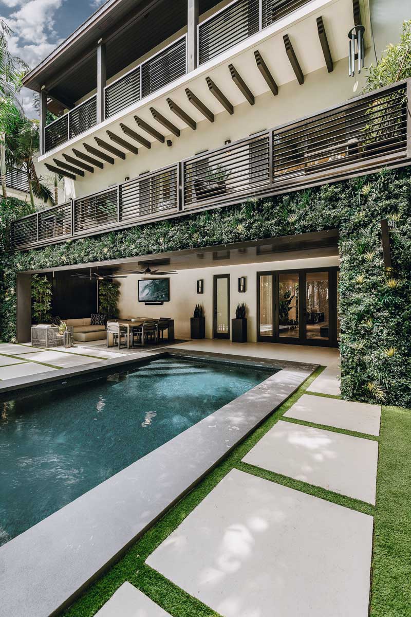 Modern backyard with sleek pool, concrete pavers, lush greenery, and vertical garden hardscapes around a stylish patio area