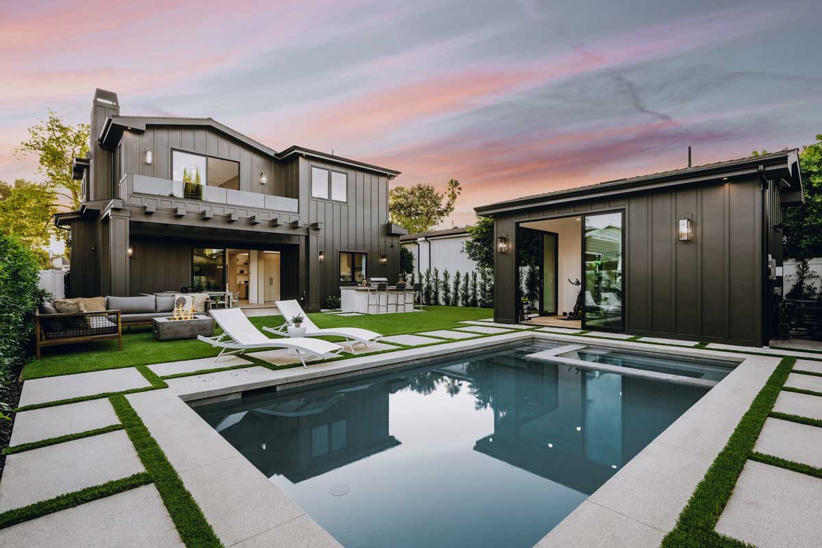 Modern backyard with sleek hardscapes, a pool, lounge chairs, and a dark-toned house with a detached pool house