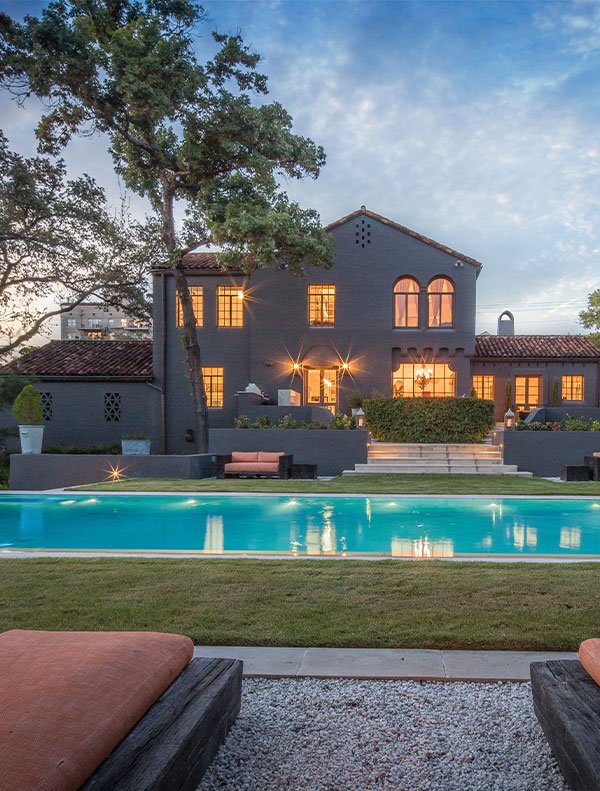 Large house featuring a pool and two lounge chairs, showcasing beautiful hardscapes in the backyard