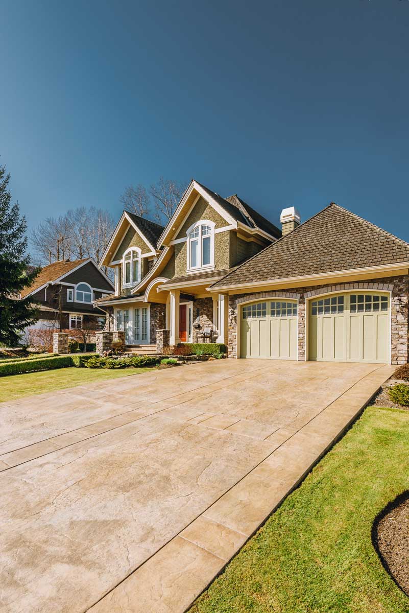 Large home featuring a spacious driveway and garage, showcasing beautiful hardscapes in the front yard