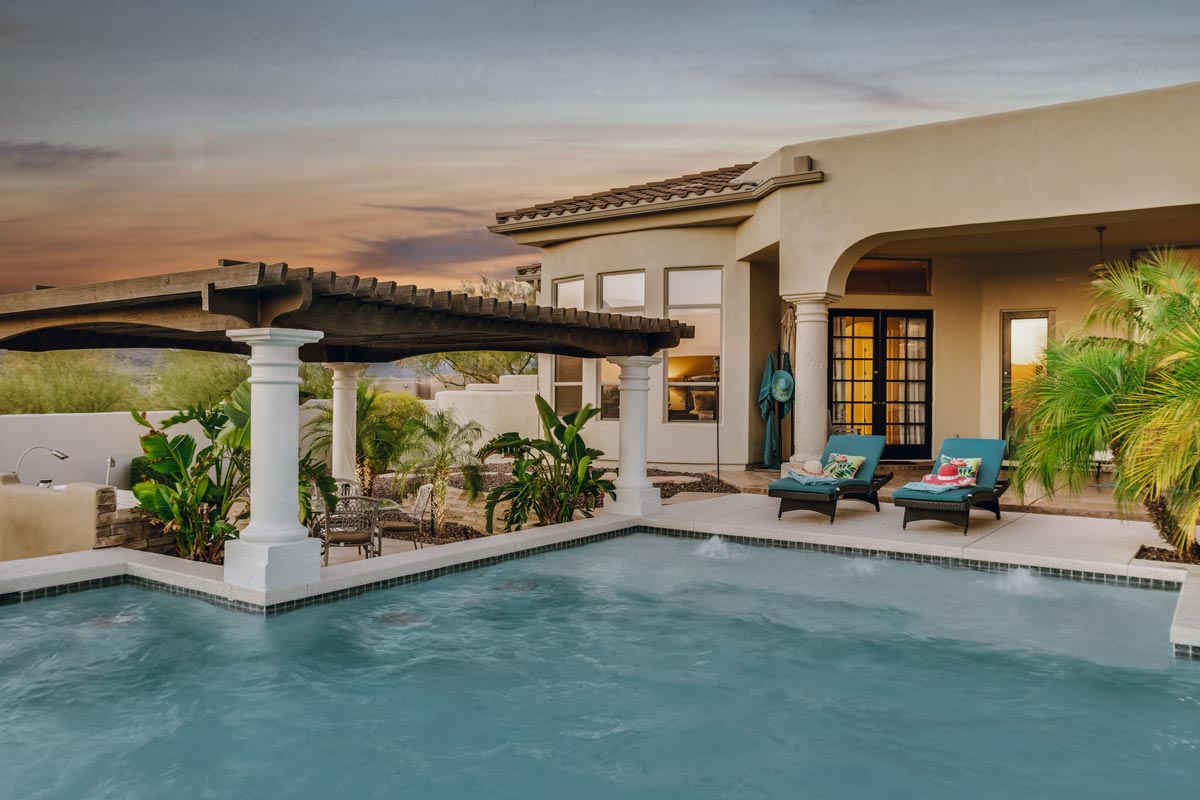 Hardscapes surround a serene pool and patio area, beautifully illuminated by a stunning sunset