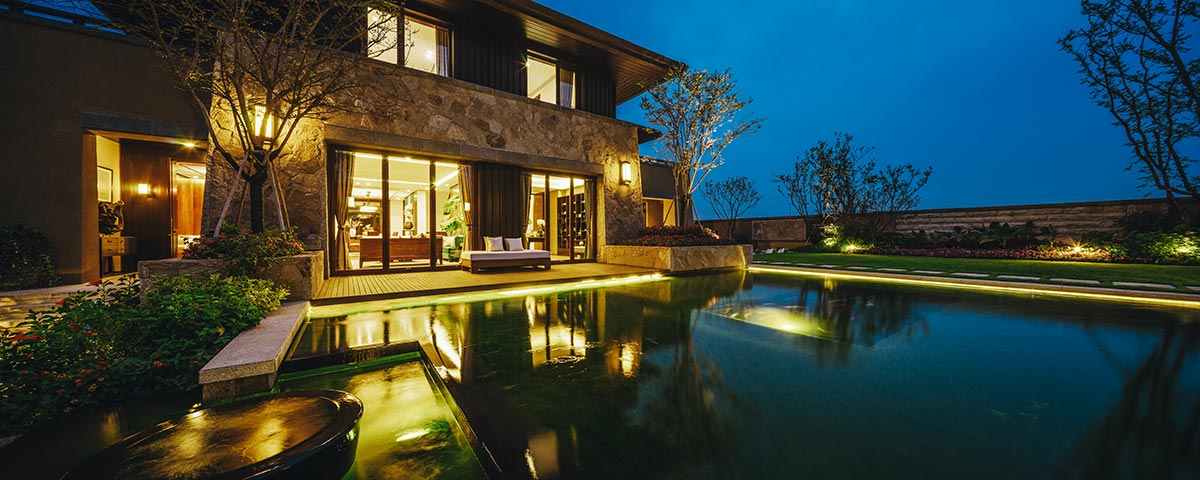 Serene house with a pool illuminated at night, showcasing beautiful hardscapes and a tranquil atmosphere