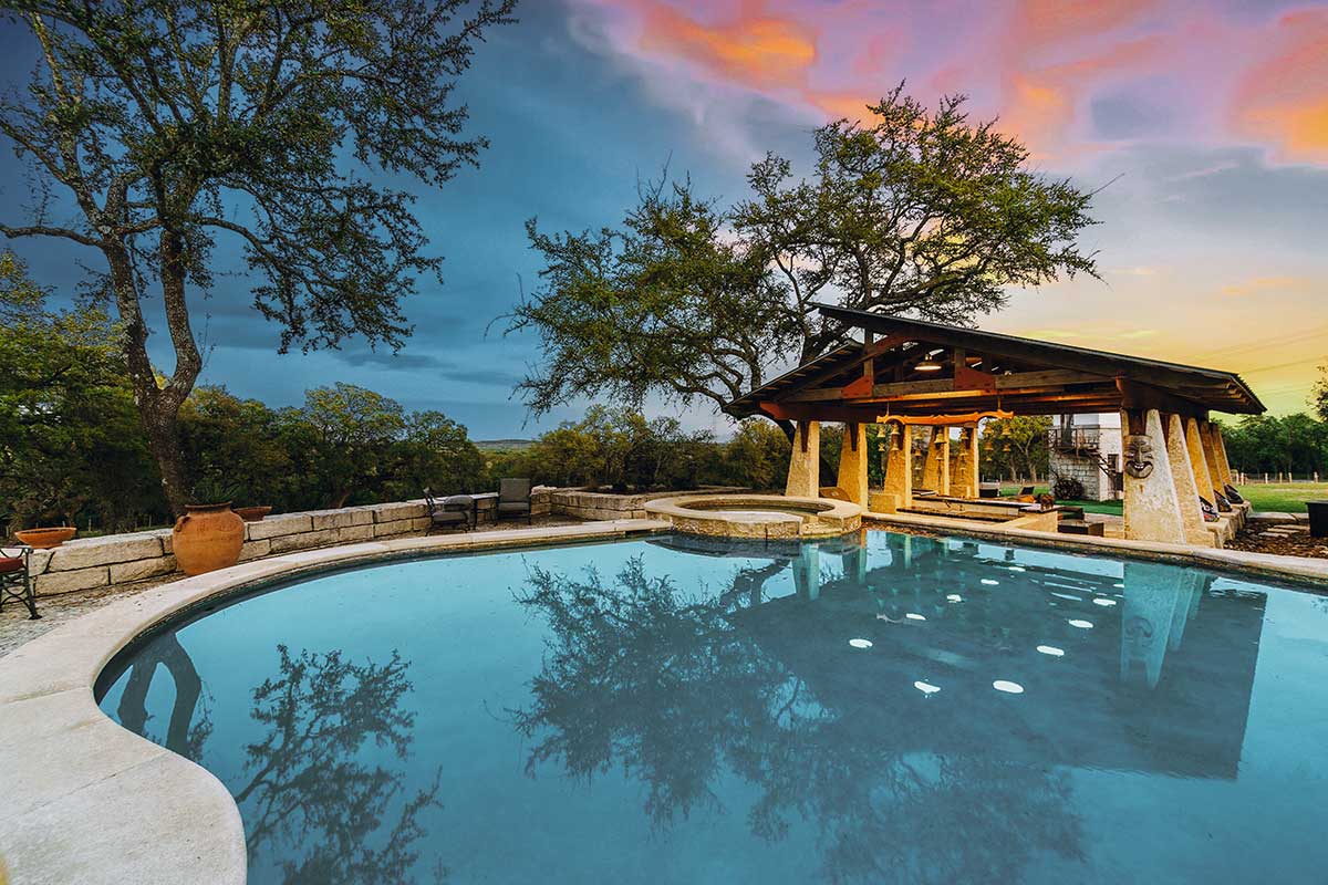 Serene pool with a gazebo at sunset, showcasing beautiful hardscapes and a tranquil atmosphere