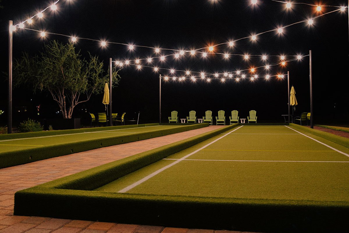 Beautifully lit bocce ball court at night, surrounded by lush lawn and elegant hardscapes