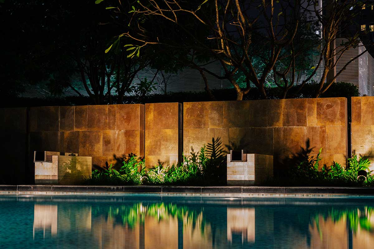 Serene night pool scene surrounded by trees and a wall, showcasing beautiful hardscapes under the stars