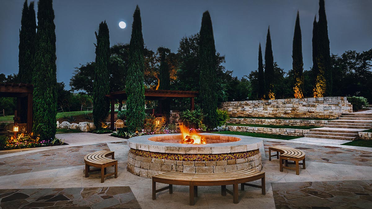 Cozy fire pit surrounded by a stone patio, perfect for gatherings under the night sky Hardscapes enhance the ambiance