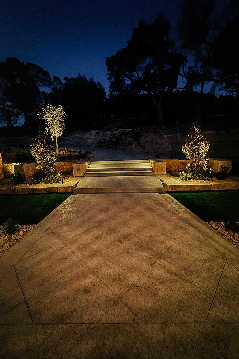 Beautifully lit walkway at night, surrounded by trees and bushes, showcasing stunning hardscapes