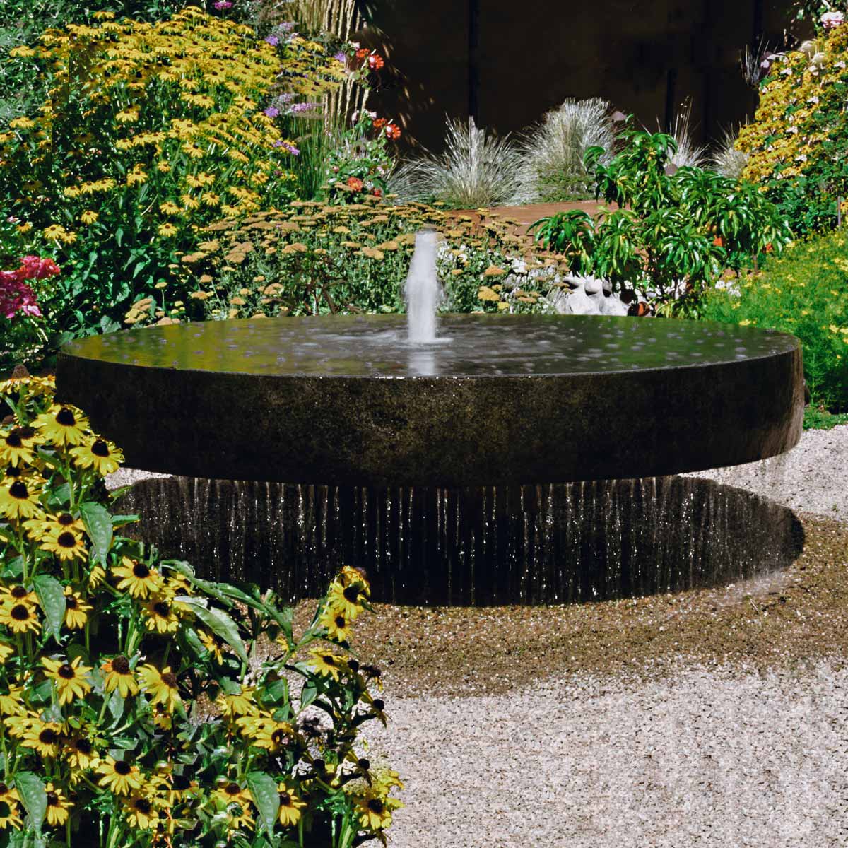 Circular fountain in a vibrant garden, surrounded by colorful flowers, showcasing beautiful water features