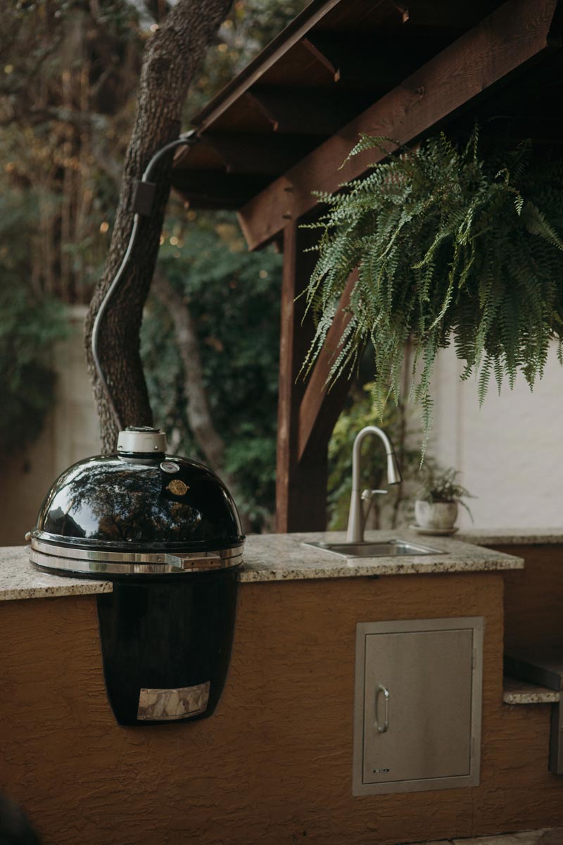 Grill sits on a wooden counter beside a tree, showcasing a cozy outdoor kitchens vibe