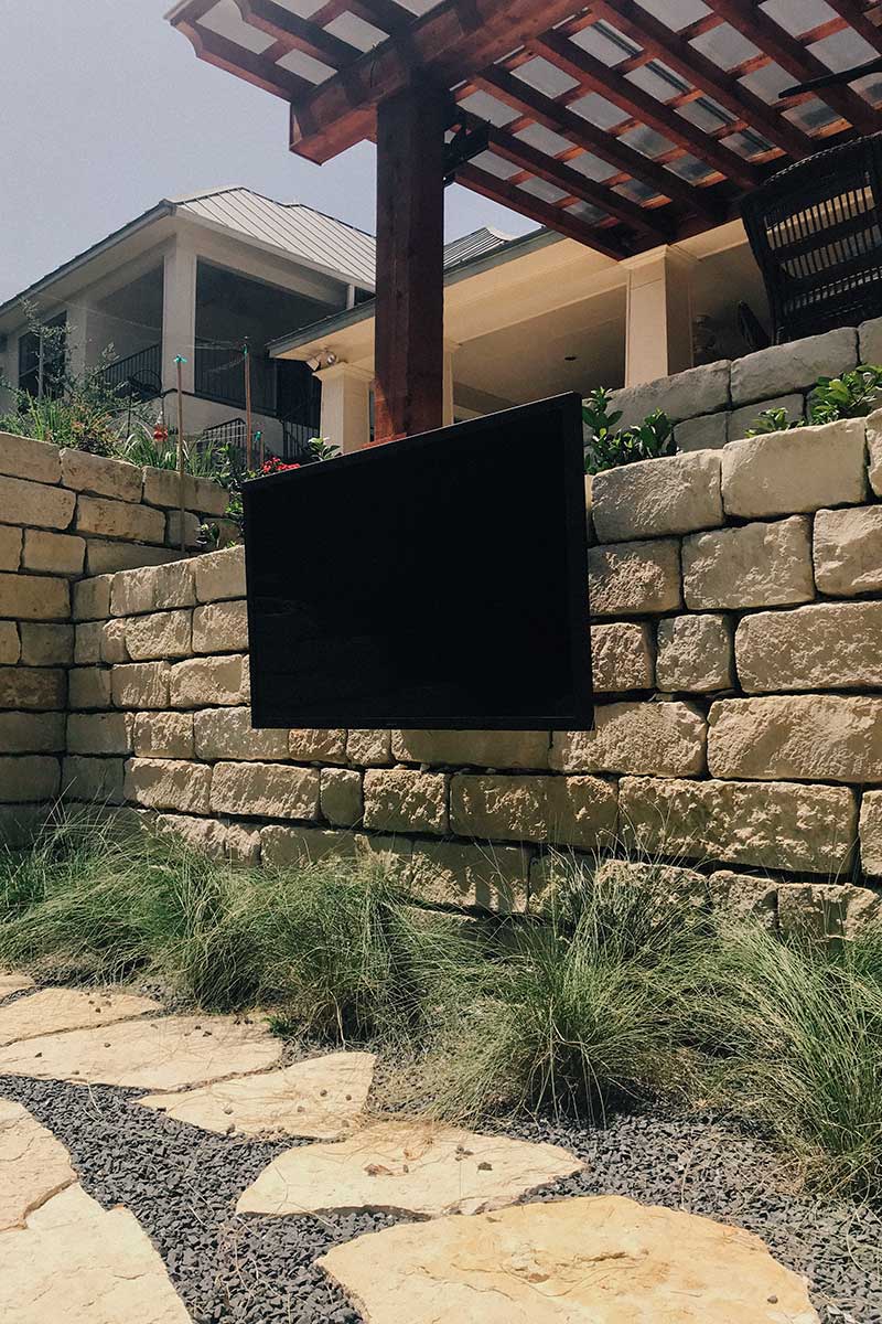 TV mounted on a stone wall, set in a cozy backyard, perfect for outdoor movie nights