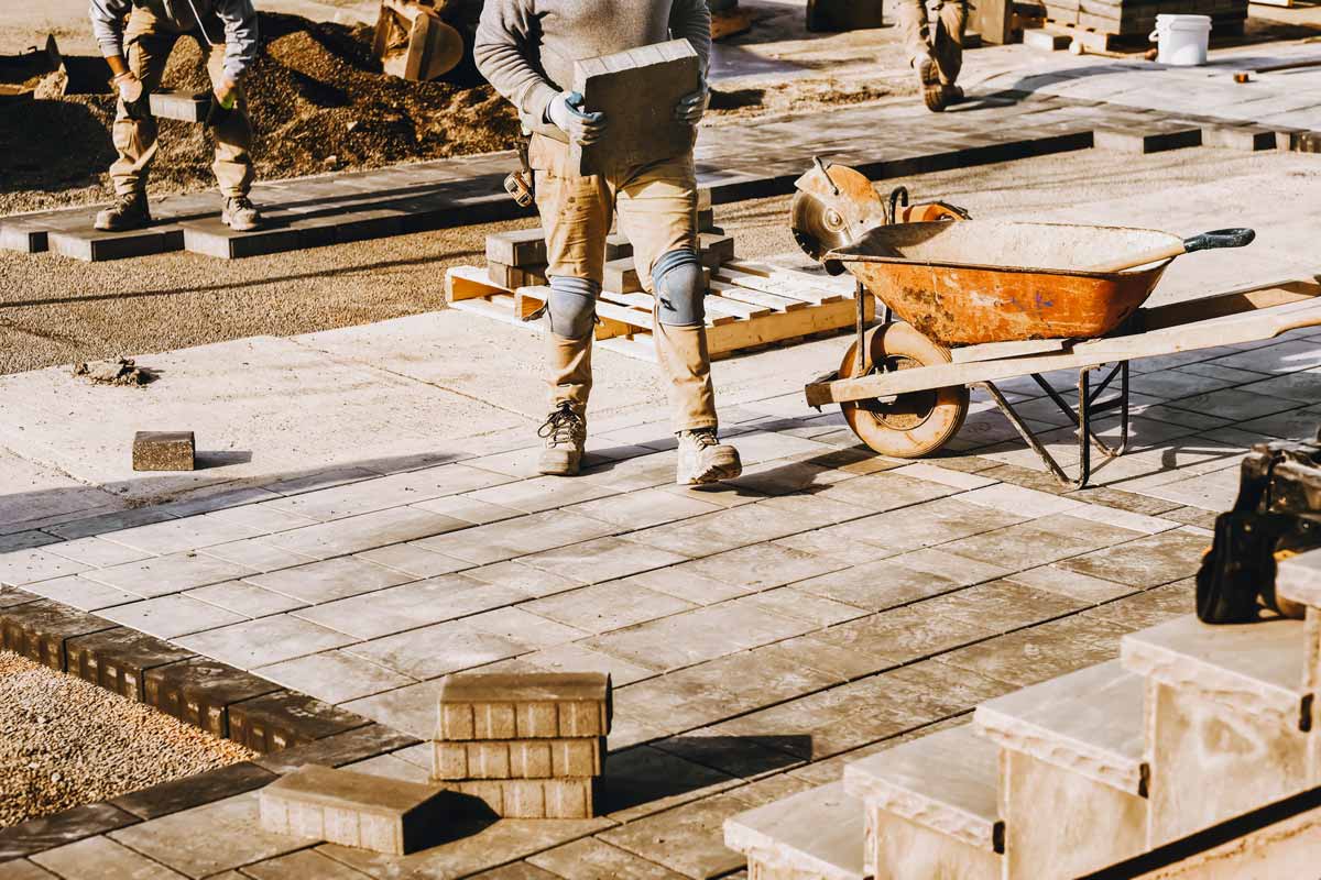 Man stands on a brick patio, holding a brick, showcasing the beauty of Hardscapes in outdoor design