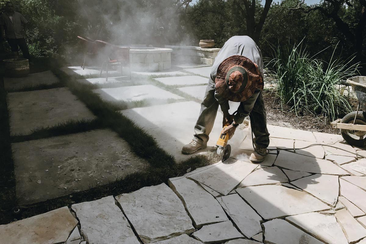 cut Man skillfully uses a power tool to cut stone for Hardscapes, shaping the material with precision