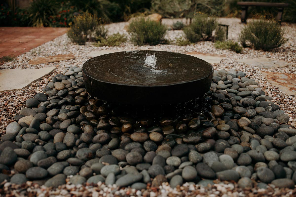 Black circular fountain sits amidst rocks and gravel, showcasing elegant water features in a serene setting