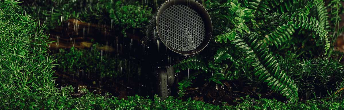 Speaker standing alone in lush green grass with rain, evoking a moody atmosphere