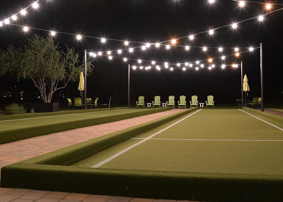 Well-lit bocce ball court on a lush lawn, glowing under the night sky, inviting for a game