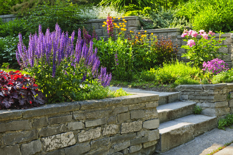 Stone retaining wall adorned with vibrant flowers and lush plants, adding charm to the landscape