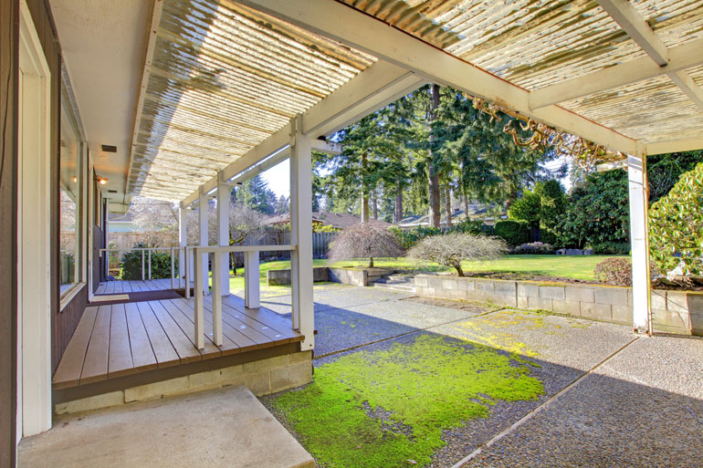 Cozy covered porch with a wooden floor overlooks a lush green lawn, perfect for relaxing outdoors