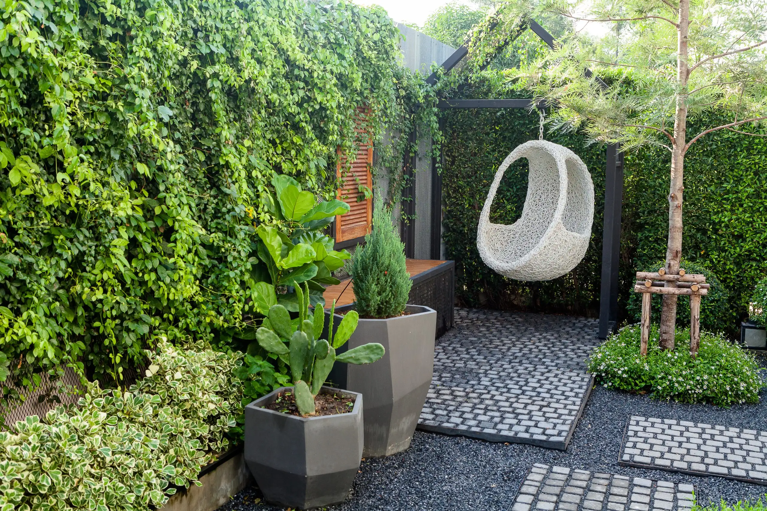 Cozy outdoor seating area with a hanging egg chair, potted plants, and a stone pathway