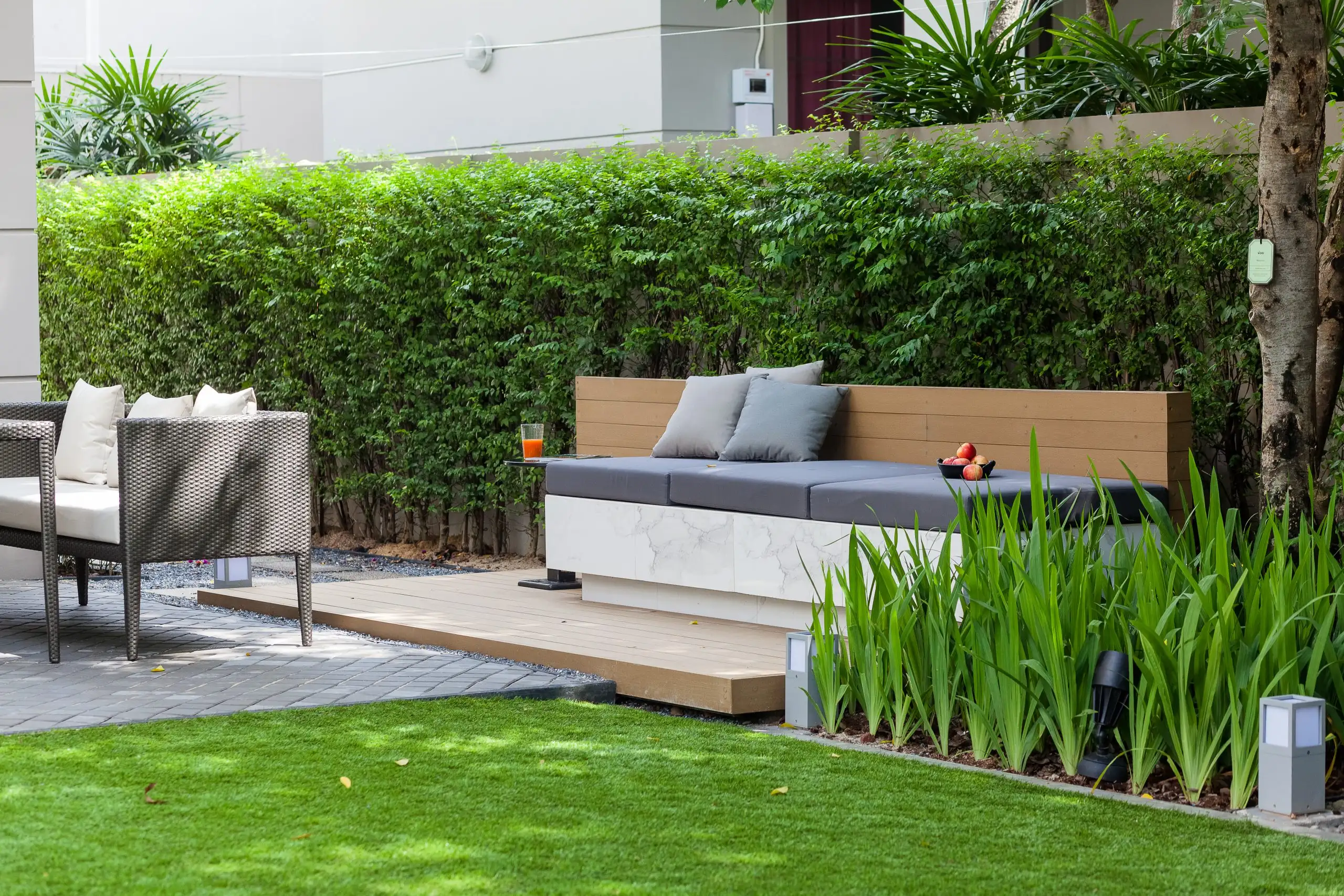 Modern outdoor seating area with marble bench, wooden backrest, and plush cushions Hardscapes add to the lush greenery