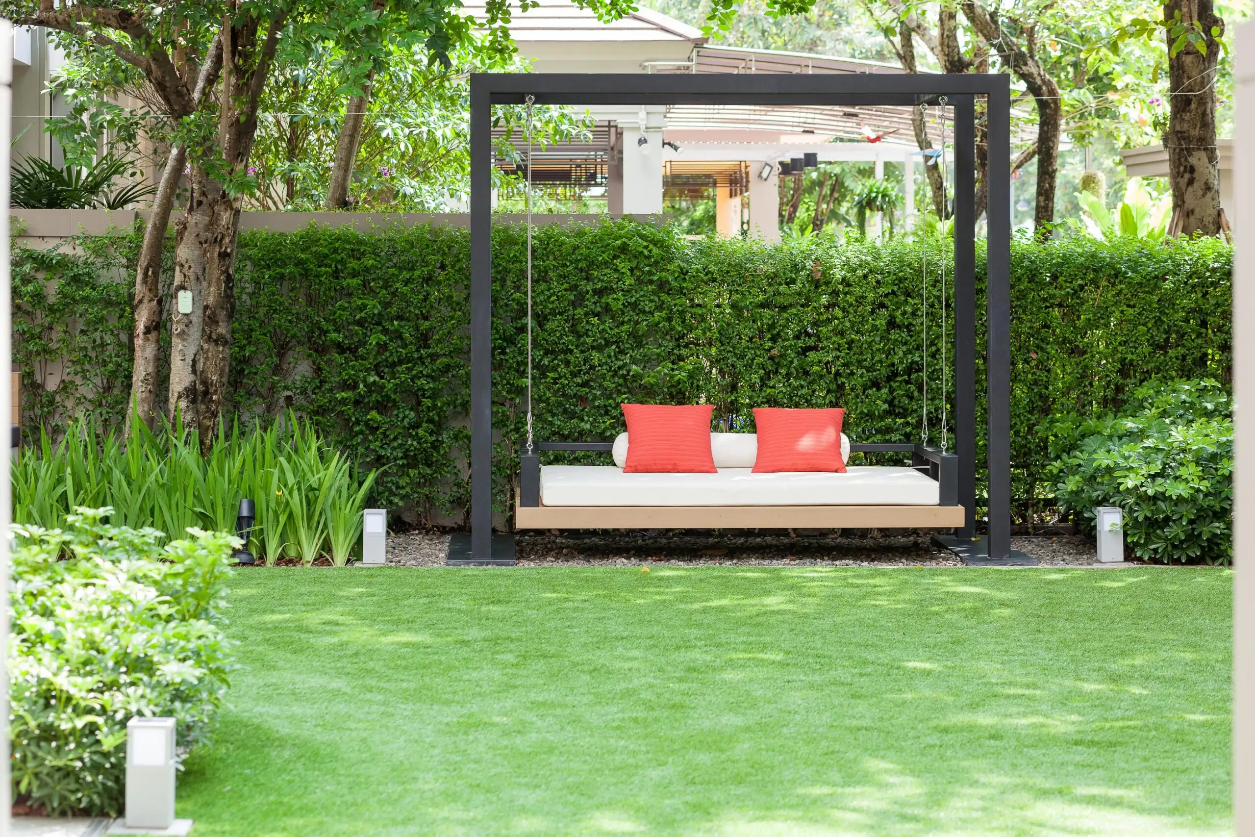 Modern outdoor daybed with red pillows, surrounded by lush greenery and manicured Softscapes in a serene garden