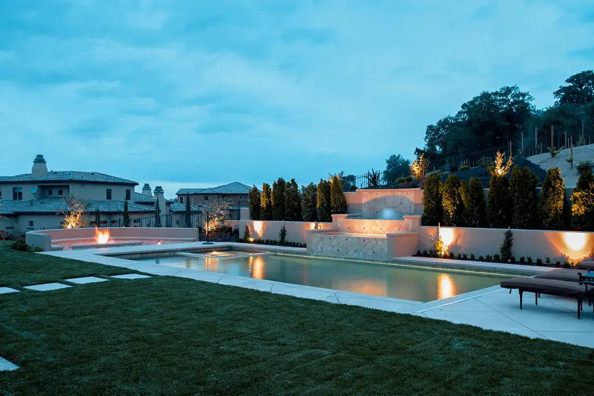 Luxurious backyard featuring a pool and lighting that highlights the Hardscapes, creating an elegant outdoor space