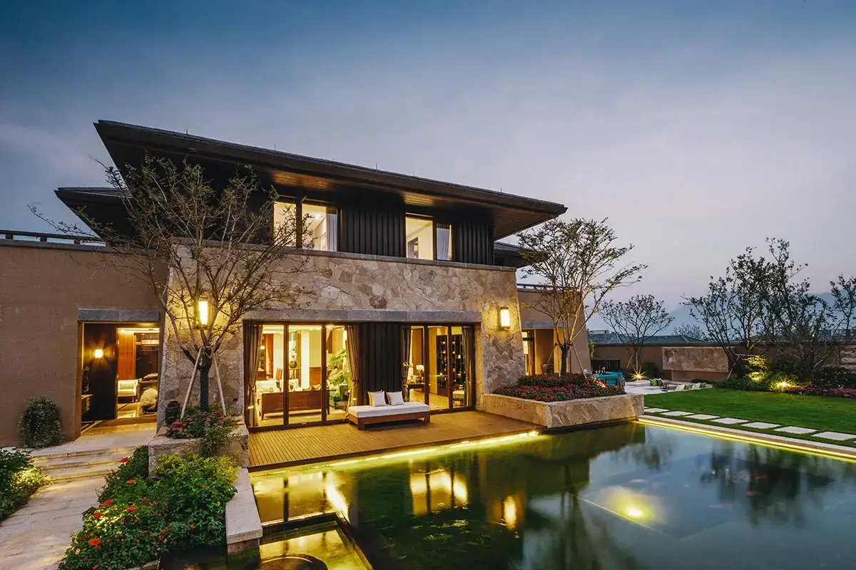 Modern home with stone cladding, featuring a backyard pond with illuminated hardscapes pathways and manicured gardens