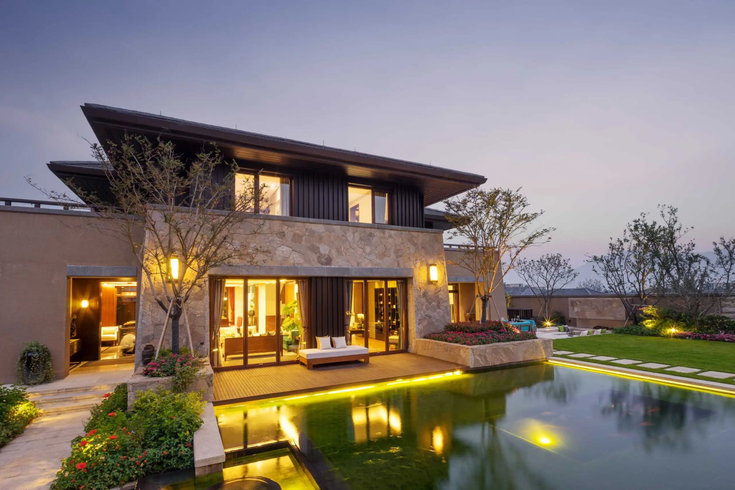 Modern home at dusk with softscapes of vibrant plants surrounding a reflective pond, illuminated by soft lights