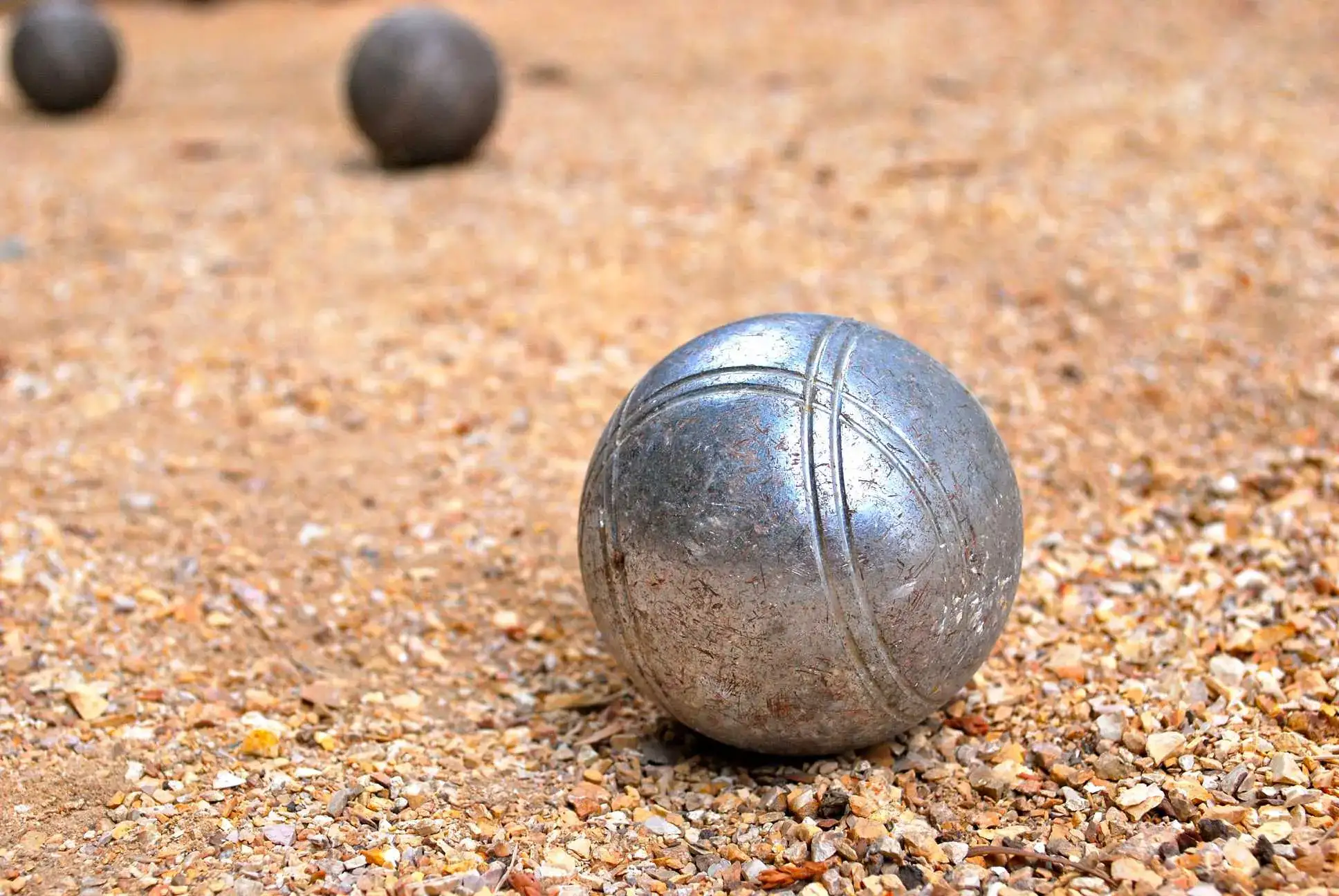 Close-up of a metallic bocce ball on a gravel court, set in a softscapes environment with blurred background elements