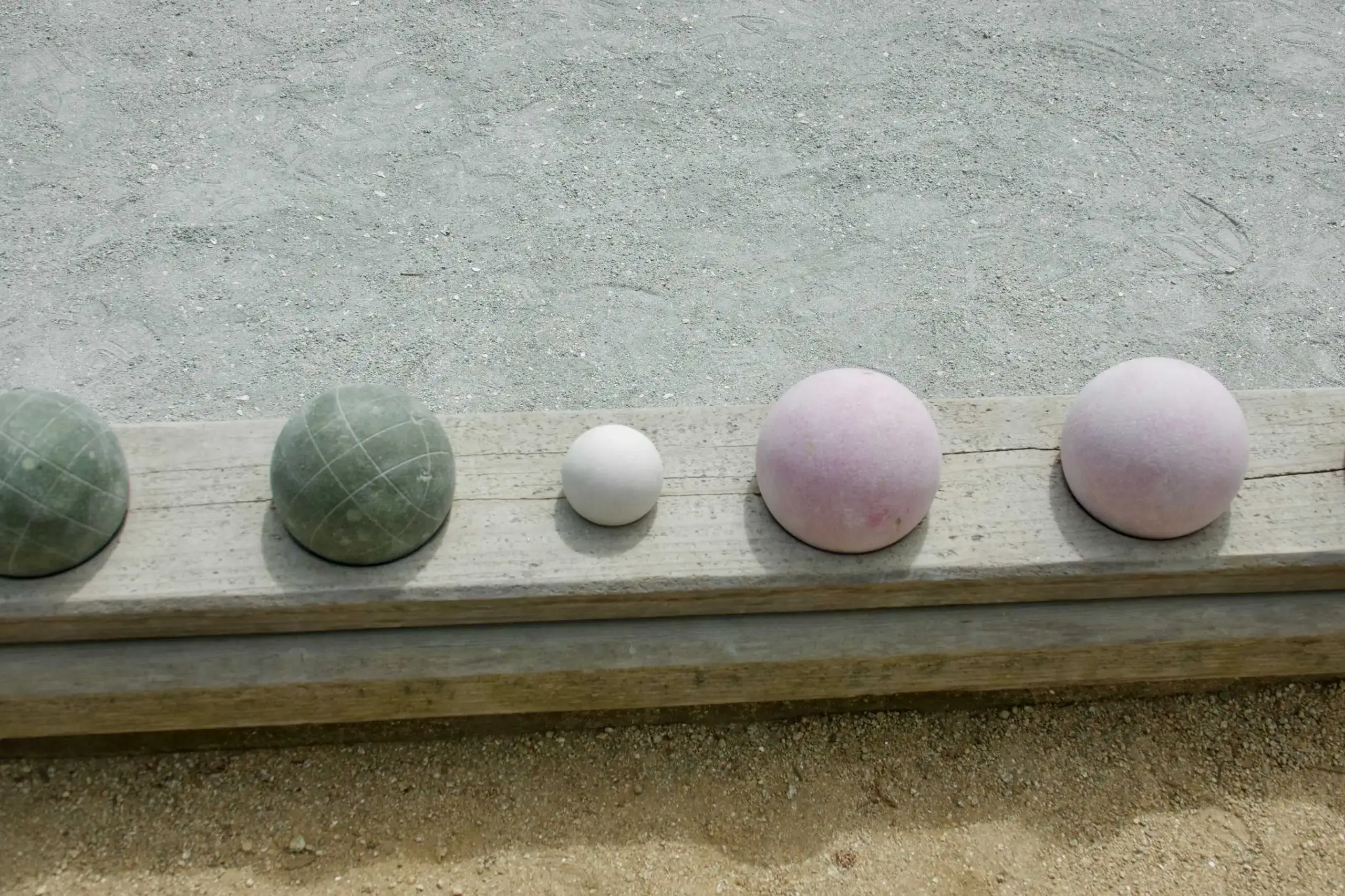 Bocce balls on a wooden ledge by a sandy court, surrounded by softscapes, highlighting a natural landscape setting