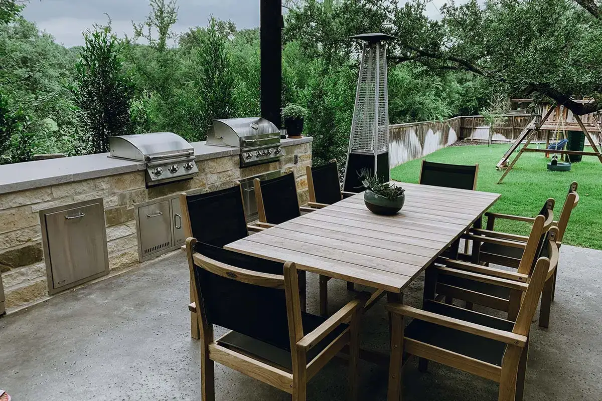 Outdoor kitchens with stone counters, built-in grills, a large wooden dining table, and a patio heater