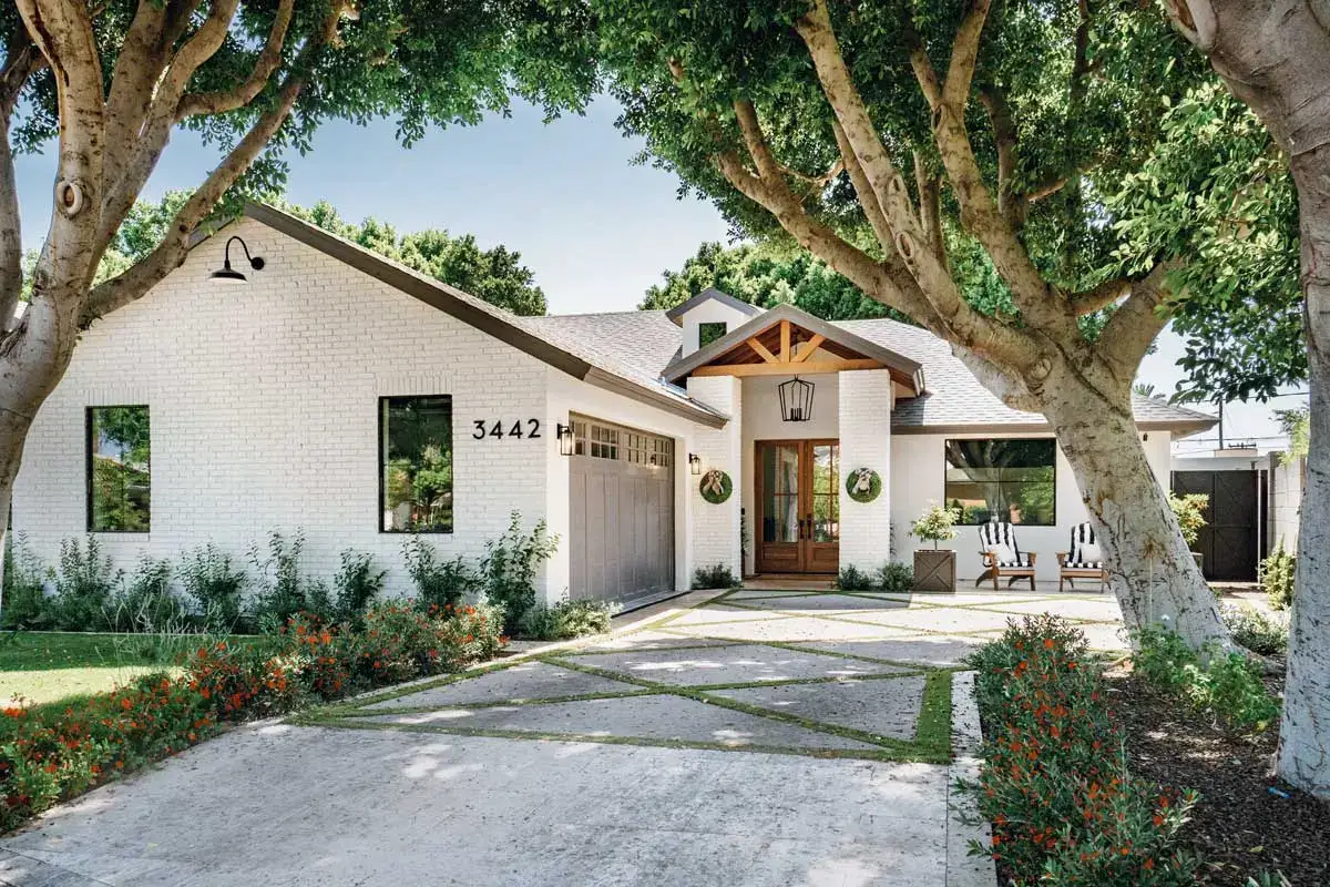 Charming home with a concrete driveway featuring grass inlays, surrounded by mature trees and lush landscaping