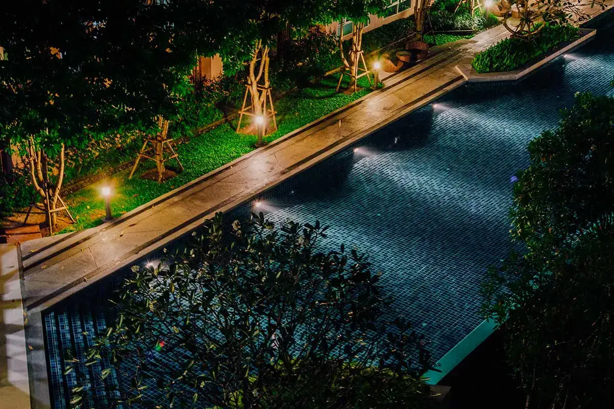 Elegant pool area with stone hardscapes, ambient lighting, and lush trees, creating a serene nighttime atmosphere