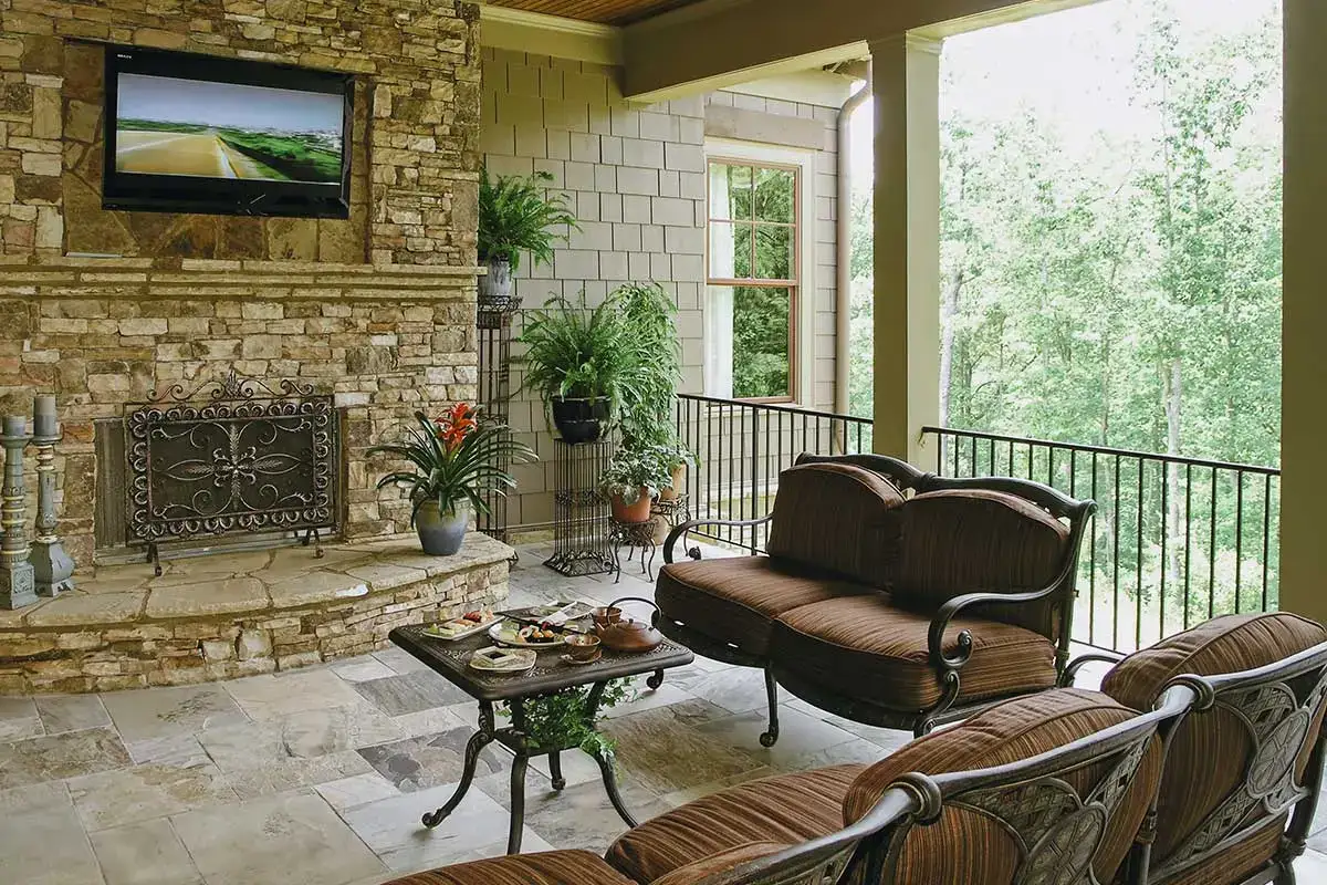 Cozy patio with stone hardscapes featuring a fireplace, TV, and elegant seating, surrounded by lush greenery