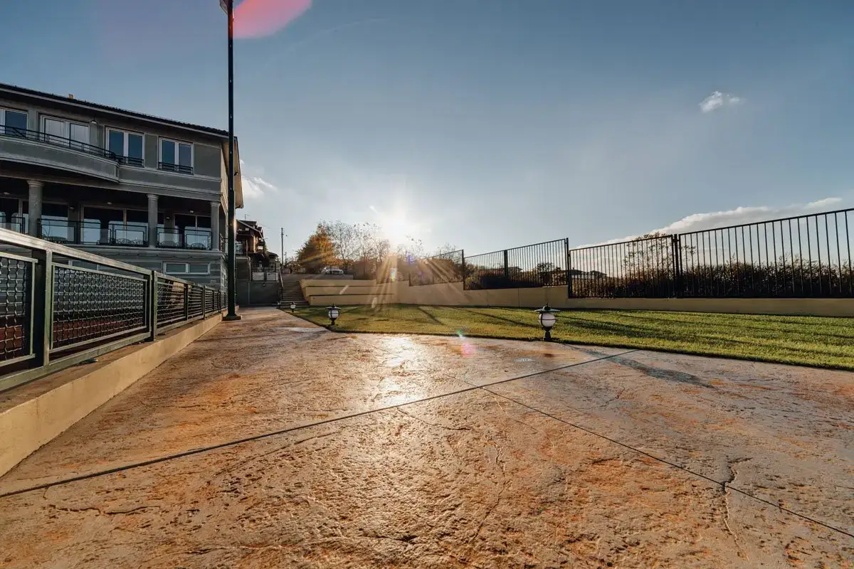 Stamped concrete hardscapes with modern railings, grassy areas, and a sunlit view of a multi-story home