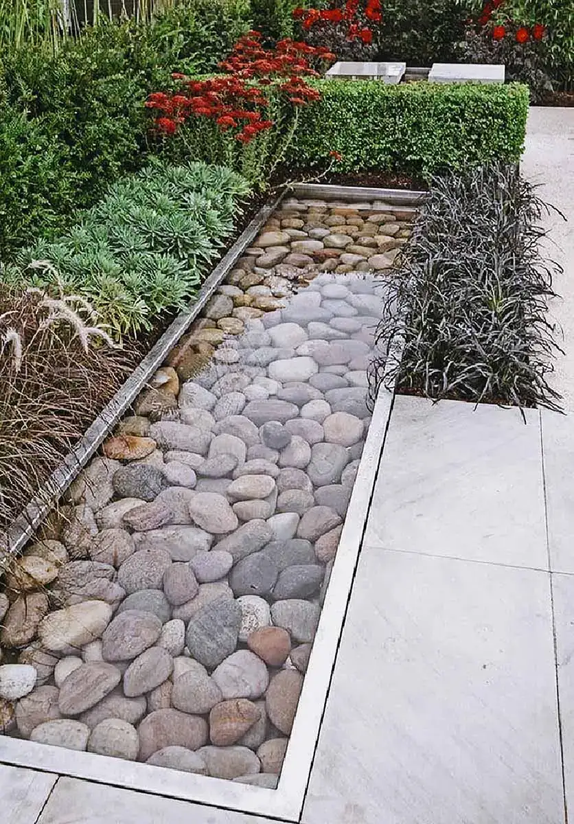 Modern water features with smooth river rocks, framed by lush plants and clean, minimalist landscaping design