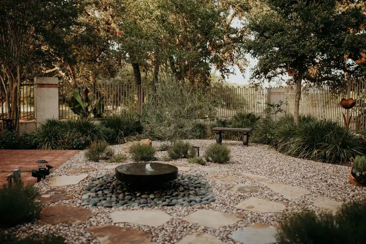 Peaceful courtyard with a water features, surrounded by flagstone hardscapes, gravel, and lush greenery